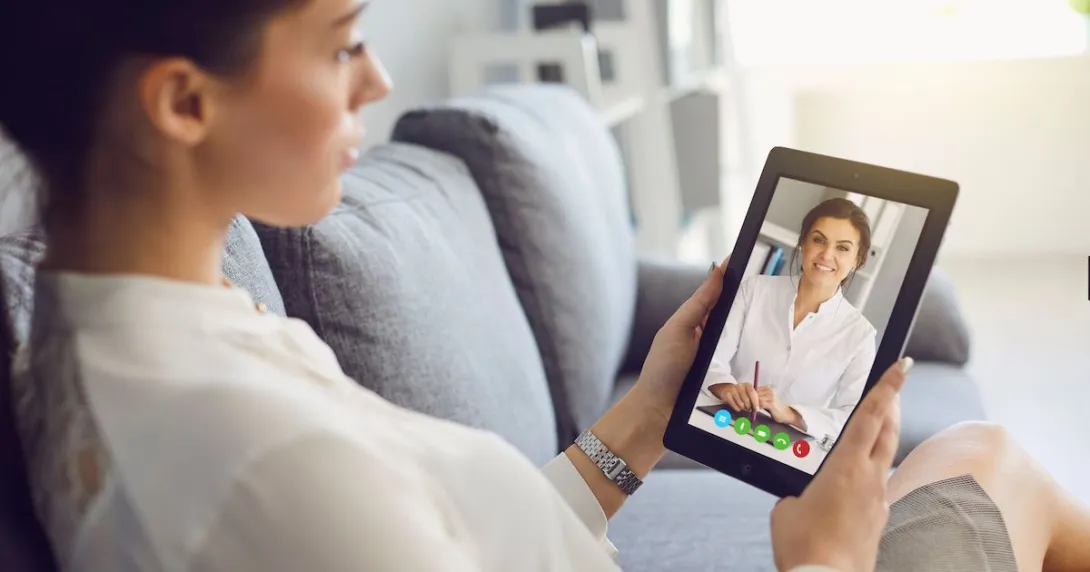 Woman sits on a couch with her tablet during a mental health visit